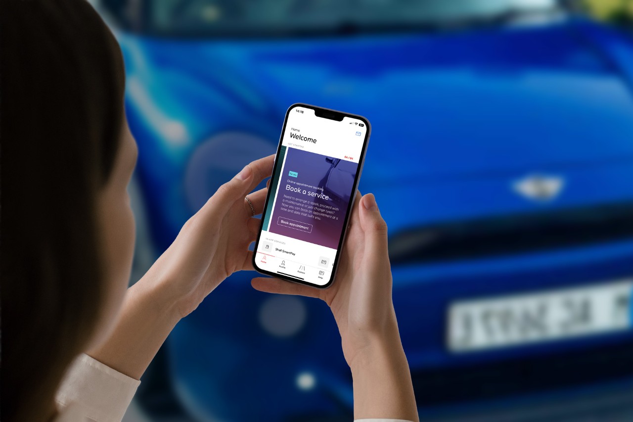 A person uses the Alphabet corporate mobility app on a smartphone, booking a vehicle service in front of a blue BMW Group car. The image illustrates digital convenience in managing fleet solutions.