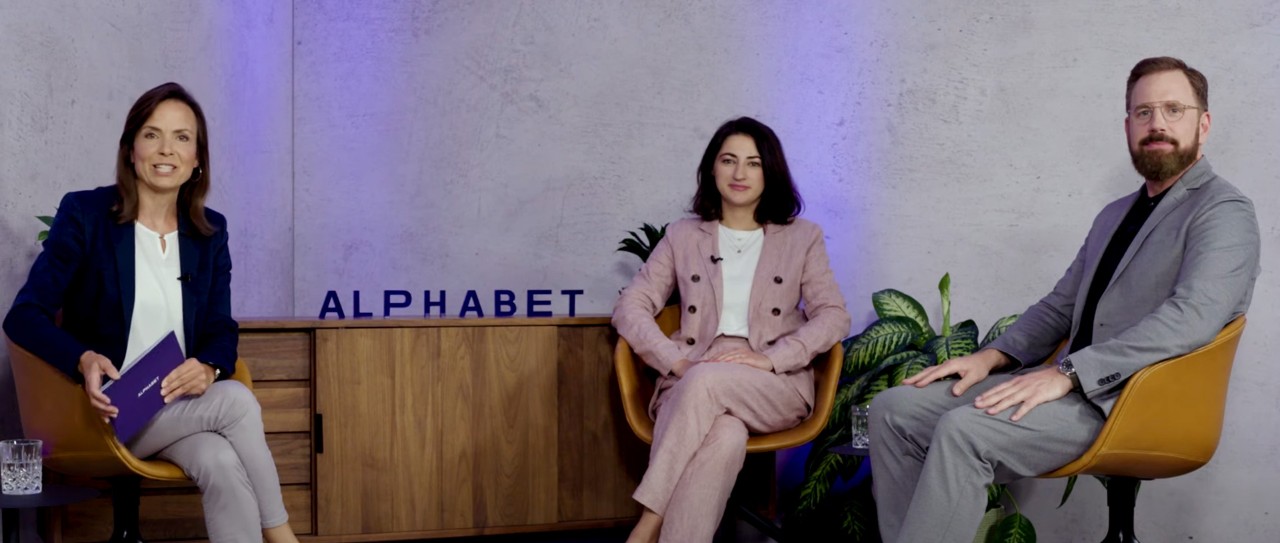 Three professionals engage in a panel discussion in a modern studio setting at Alphabet, seated in front of branded decor and vibrant lighting.