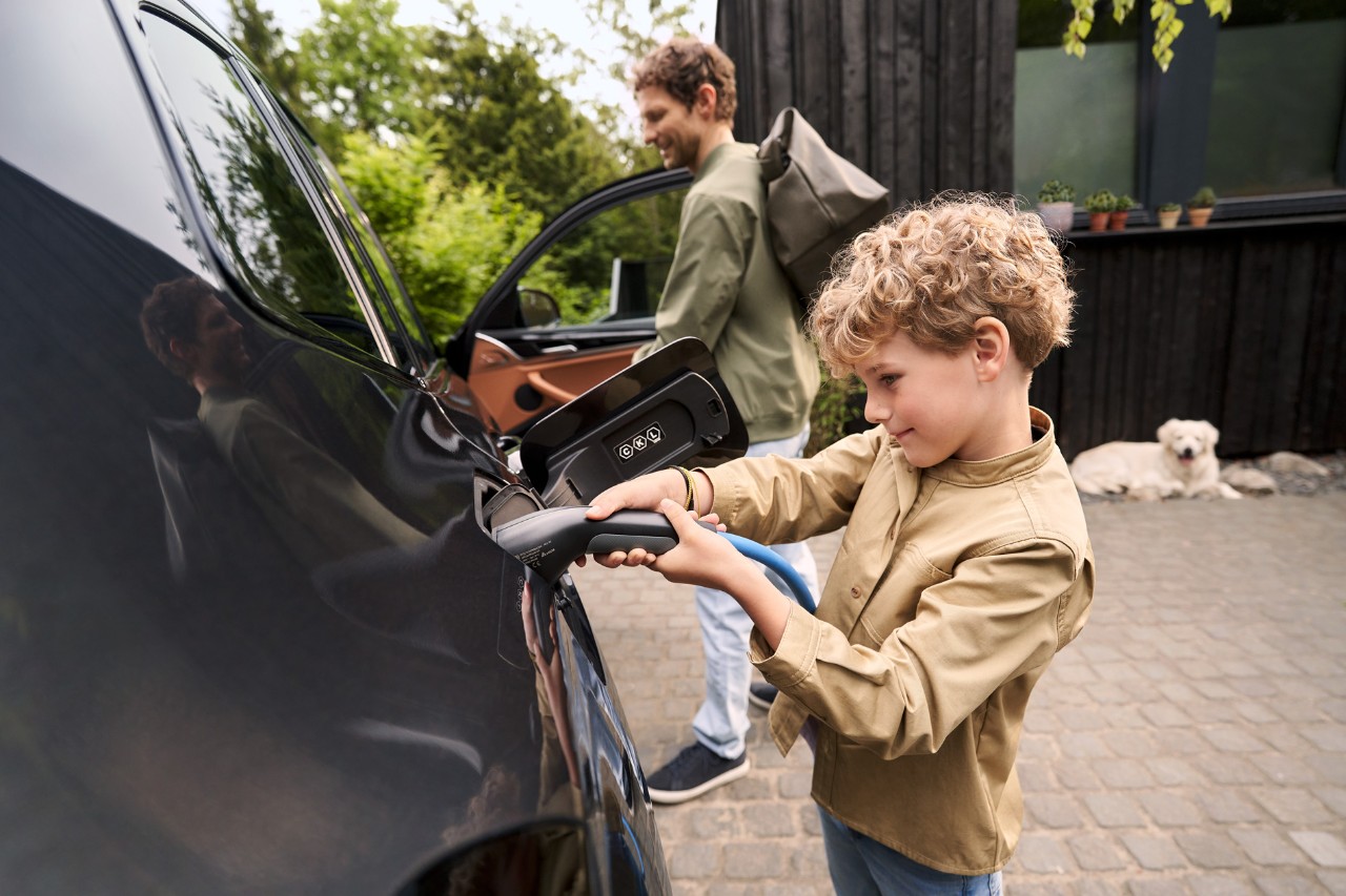 Boy holding EV electric charger in to car parent and dog behind him.