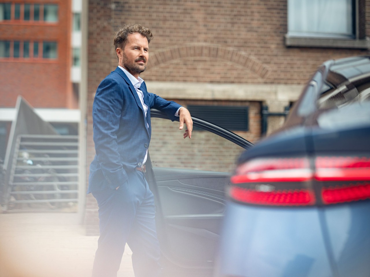 Man rests his arm on the driver’s door of a car.