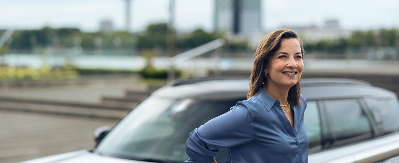 Woman leans against a railing with a white MINI car visible in the background.