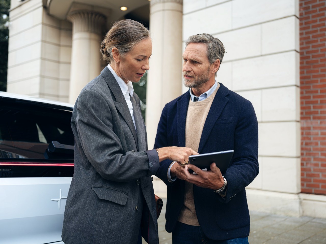 Woman talks to a man and points to the tablet in his hand.
