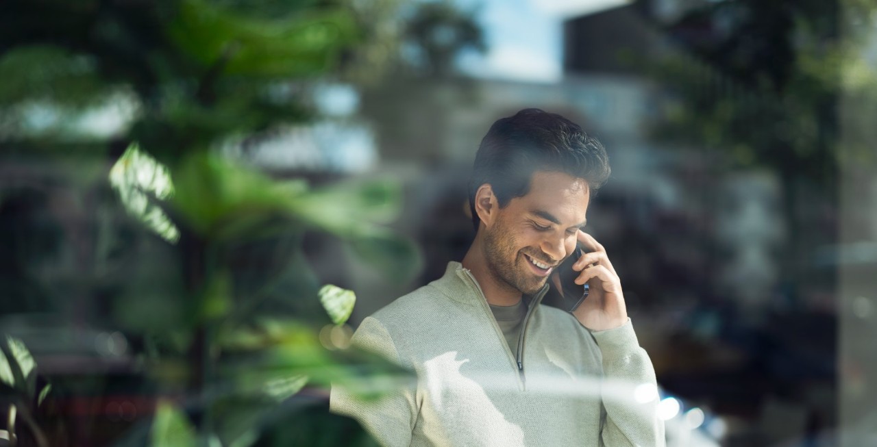 Man talking on a smartphone behind a glass pane.
