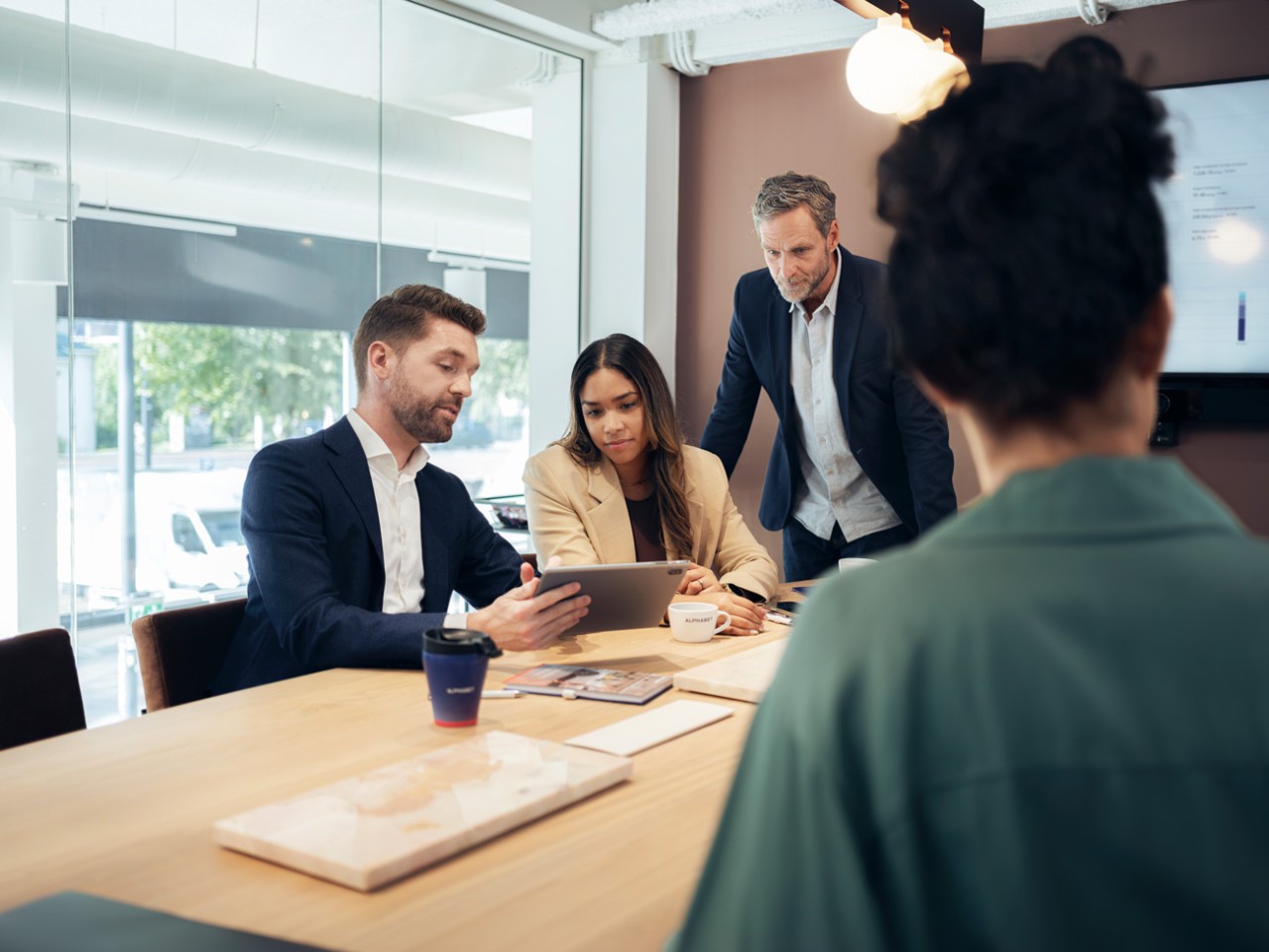 Three people having a meeting with a tablet in a modern office with natural light and a view of trees.